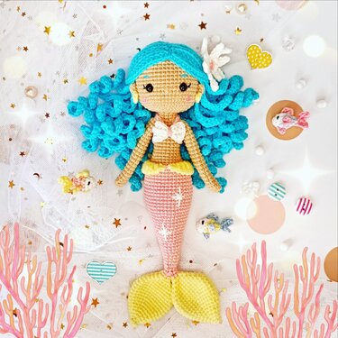 Amigurumi-Meerjungfrau mit aquablauen Locken, weißem Muscheltop und rosa-gelbem Schwanz, kunstvoll gehäkelt