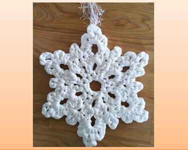 Weiße gehäkelte Schneeflocke mit Aufhängeschlaufe auf Holzuntergrund