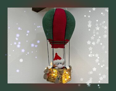 gehäkelter grüner und roter Heißluftballon mit Amigurumi-Weihnachtsmann im Korb und Lichterkette