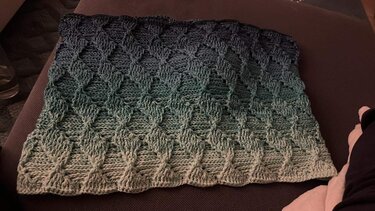 Gehäkelter Loop in Grün- und Petrolverlauf mit Rautenmuster auf dunklem Untergrund