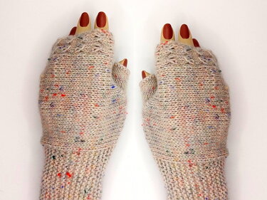 Beige gestrickte fingerlose Handschuhe mit bunten Sprenkeln an Modellhänden