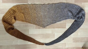 Gehäkeltes Dreieckstuch mit Ombre-Farbverlauf in Gold und Grau auf hellem Holzboden