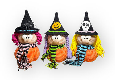 Drei gehäkelte Amigurumi-Hexen mit orangefarbenen Kürbissen, bunten Haaren und verzierten Hüten