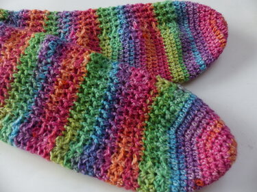 Nahaufnahme gehäkelte Socken in bunten Regenbogenstreifen mit strukturierter Maschenfolge und abgerundeter Spitze