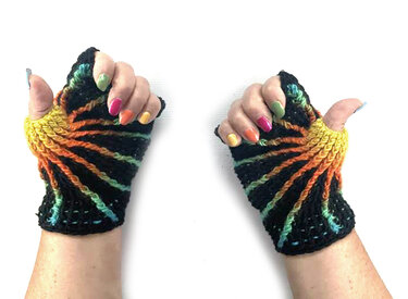 Zwei Hände mit gehäkelten, fingerlosen Handschuhen in Schwarz und strahlenförmigen Regenbogenstreifen, Daumenöffnung sichtbar.