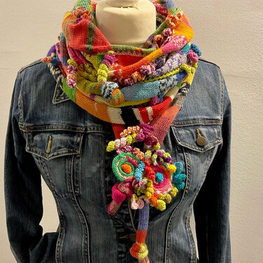 Bunter gestrickter Loop-Schal mit Zierknoten, getragen an einer Schaufensterpuppe über einer Jeansjacke.