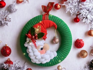 Green crocheted door wreath with 3D Santa face, slouchy red hat, bobble-textured white beard and hanging bauble