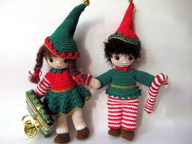 Zwei gehäkelte Amigurumi-Wichtel zu Weihnachten mit Geschenk und Zuckerstange vor weißem Hintergrund