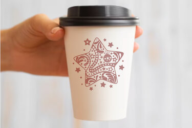 Weißer To-Go-Becher mit braunem ornamentalem Sternmotiv, gehalten in einer Hand