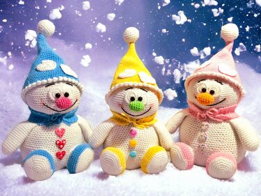 Three crocheted snowman amigurumi with blue, yellow, and pink hats and scarves sitting on snow.
