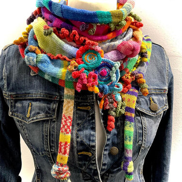 Bunter, gestrickter Loopschal mit vielen Applikationen über einer Jeansjacke auf einer Schneiderpuppe.