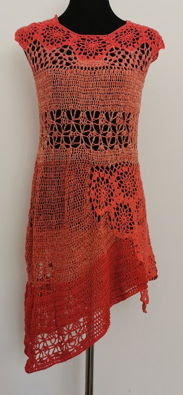 Gehäkelte korallfarbene Tunika mit runden Spitzen, Netzstreifen, floralen Motiven und schrägem Saum auf einer Schaufensterpuppe