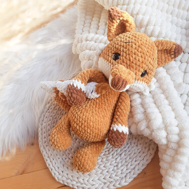 Gehäkeltes Fuchs-Amigurumi aus Plüschgarn mit weißer Schnauze auf gehäkelter Unterlage