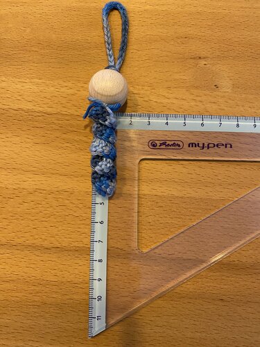 Gehäkelter blau-grauer Schlüsselanhänger mit Holzperle auf Holztisch neben Lineal