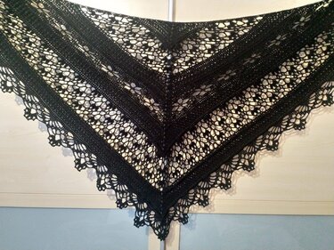 Black crocheted triangle shawl with alternating lace and solid bands and a scalloped border.