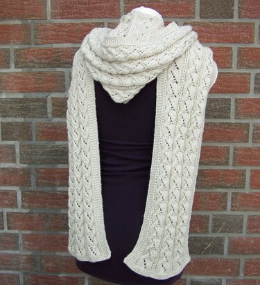 Langer cremefarbener gestrickter Kapuzen-Schal mit Zopfmuster auf einer Schaufensterpuppe vor Backsteinwand