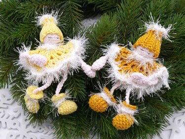 Zwei gehäkelte gelbe Engelfiguren mit flauschigen Kanten und Bommel-Schuhen auf Tannenzweigen