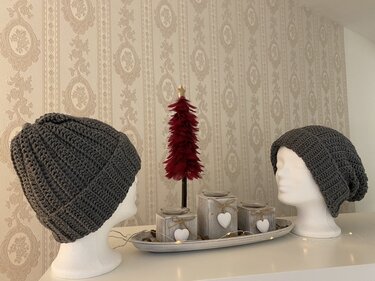 Zwei dunkelgraue gehäkelte Mützen auf weißen Schaufensterköpfen neben dezenter Tischdekoration