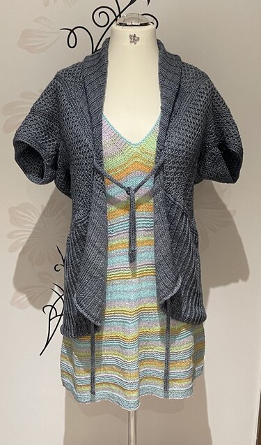 Dunkelgrauer kurzärmliger Seelenwärmer über pastellgestreiftem Stricktop auf einer Schneiderpuppe.