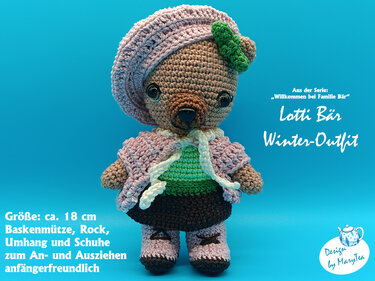 Gehäkelter brauner Teddybär Lotti mit rosa Baskenmütze, Umhang und Rock vor blauem Hintergrund.