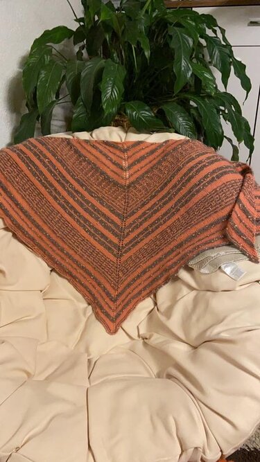 Gestricktes dreieckiges Tuch mit orange-braunen Streifen auf einem cremefarbenen Sessel