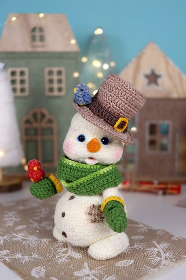 Crocheted snowman amigurumi with a brown top hat, blue and red birds, green scarf and mittens.