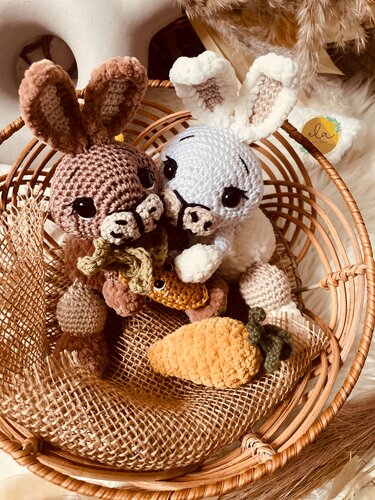 Zwei kleine Amigurumi-Hasen (braun und weiß) mit gehäkelten Möhren in einem geflochtenen Korb