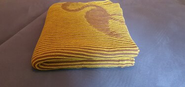 Folded yellow and brown knitted blanket with a large dark brown heart motif on a dark surface.