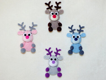 Four small colorful crocheted reindeer decorations arranged on a light background, suitable for keychains and ornaments.