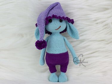 Gehäkelte Amigurumi-Figur in Hellblau und Lila mit Zipfelmütze und großen Ohren auf weißem Hintergrund