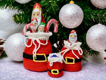 Three red crocheted Santa bags filled with chocolates and candy canes in front of a decorated Christmas tree.
