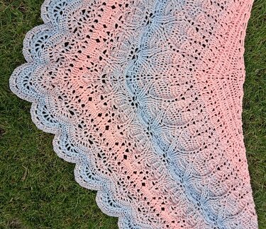 Gehäkeltes dreieckiges Tuch in Rosa bis Grau mit Spitzenmuster und Muschelkante auf Gras