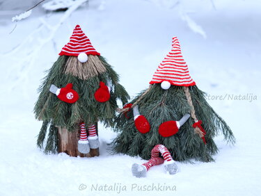 Zwei Weihnachtswichtel aus Tannenzweigen mit rot-weiß gehäkelten Mützen und Fäustlingen im Schnee