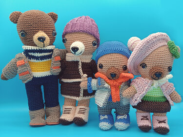 Vier gehäkelte Amigurumi-Teddys in Winterkleidung mit Mützen, Schals, Jacken und Stiefeln vor blauem Hintergrund.
