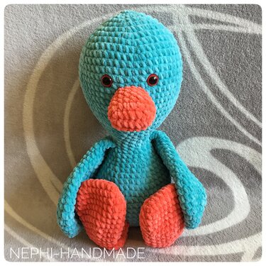 Gehäkelter Amigurumi-Vogel in Türkis mit orangefarbenem Schnabel und Füßen, frontal sitzend