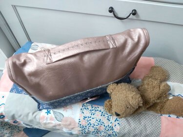 Roségoldene Utensilo-Tasche mit blauem Blumenstoff auf Patchwork-Decke neben Teddybär