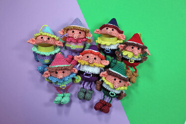 Mehrere bunte gehäkelte Amigurumi‑Wichtel mit Aufhängeschlaufen auf zweifarbigem Hintergrund