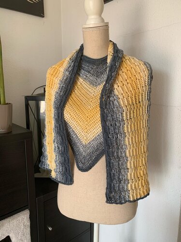 Gehäkelter Wickelschal in Gelb und Grau mit V-förmigem Chevron-Mittelteil und texturierten Seiten auf einer Schneiderpuppe.