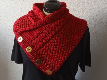 Roter gehäkelter Kragenschal mit vier goldfarbenen Knöpfen auf schwarzem Oberteil einer Schneiderpuppe.