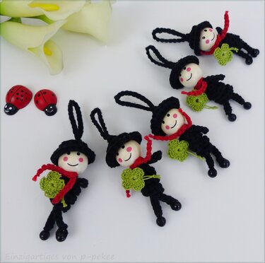 Mehrere gehäkelte Glücksbringer‑Anhänger mit Holzperlenköpfen, roten Schals und grünen Kleeblättern