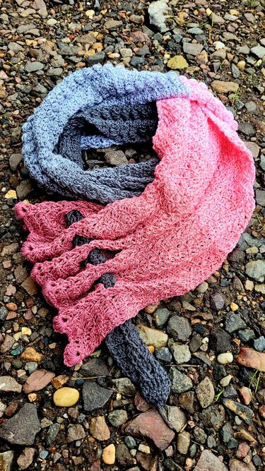 Gray-to-pink ombré triangle crochet shawl with shell stitch and scalloped edge on pebbles