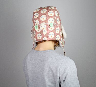 Rückenansicht einer Person, die eine rosa Ohrenklappenmütze mit Tiergesichtern und grünen Karoknöpfen trägt