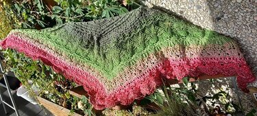 Gehäkeltes Dreieckstuch mit Farbverlauf von Grün zu Rosa, auf Terrasse neben Pflanzen ausgebreitet