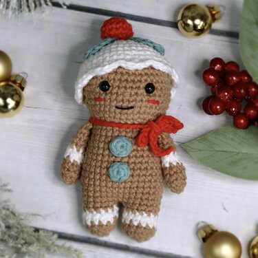 Gehäkeltes Lebkuchenmännchen-Amigurumi mit weißer Mütze, rotem Schal und türkisfarbenen Knöpfen