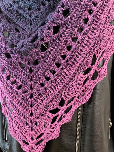 Nahaufnahme eines gehäkelten Dreieckstuchs in Lilatönen mit Lochmuster auf schwarzer Jacke