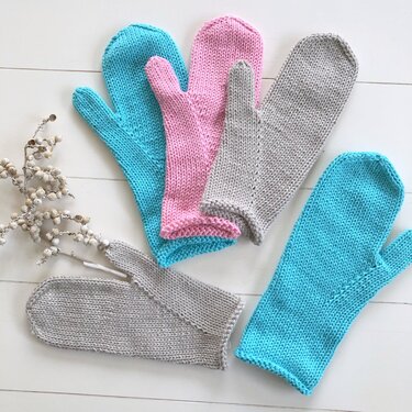 Fünf gestrickte Fäustlinge in Türkis, Rosa und Hellgrau auf hellem Holz, verschiedene Größen