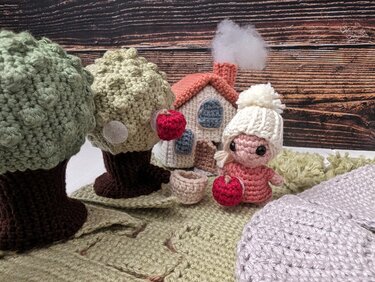 Handmade crochet amigurumi set with doll, house, and two trees on a green base.