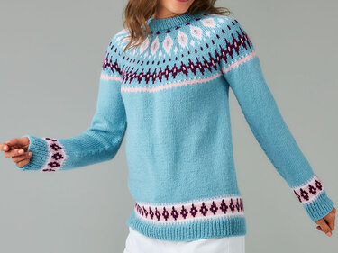 Person trägt hellblauen Strickpullover mit mehrfarbigem Fair-Isle-Muster an Passe, Ärmeln und Saum.