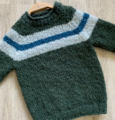 Grüner flauschiger Kinderpullover mit weißer und blauer V‑Passe auf Holzboden