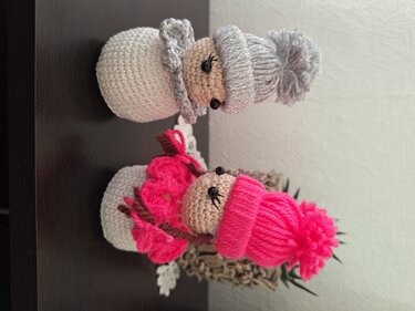 Zwei gehäkelte Engel‑Figuren mit Mützen und Flügeln, eine grau, eine pink.